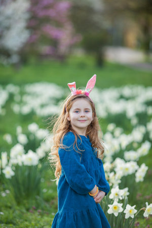 Easter. Little cute girl 5 years old with rabbit ears on the lawn of daffodils. happy child.の写真素材