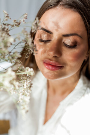 Portrait of beautiful young woman with long hair on white background with dried flowers. Shadow on the face from flowers.の写真素材