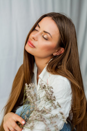 Portrait of beautiful young woman with long hair on white background with dried flowers.の写真素材
