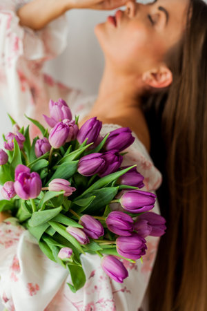Portrait of sexy beautiful young woman with long hair. Model with a bouquet of lilac tulips on white. holidays.の写真素材