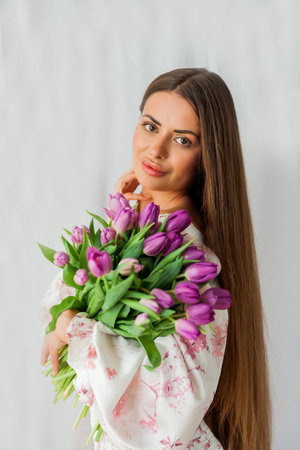 Portrait of sexy beautiful young woman with long hair. Model with a bouquet of lilac tulips on white. holidays.の写真素材