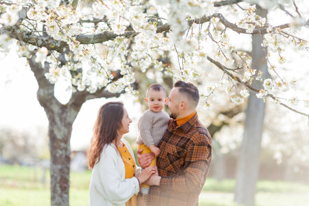 Happy young family with little son walks in blooming garden. Mom and dad with 1 year old baby.の写真素材