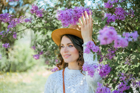 Portrait of beautiful young dark-haired woman with blue eyes in hat near the blooming. Happy model with curly hair.の写真素材