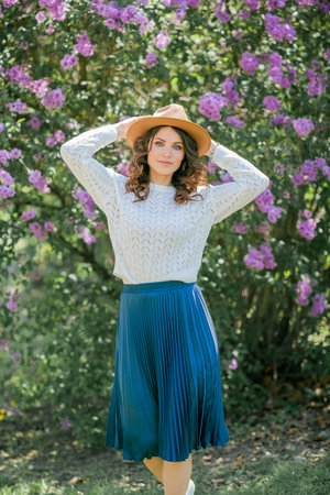 Portrait of beautiful young dark-haired woman with blue eyes in hat near the blooming. Happy model with curly hair.の写真素材