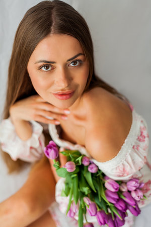 Portrait of sexy beautiful young woman with long hair. Model with a bouquet of lilac tulips on white. Spring. holidays.の写真素材
