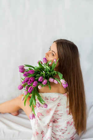 Portrait of sexy beautiful young woman with long hair. Model with a bouquet of lilac tulips on white. Spring. holidays.の写真素材