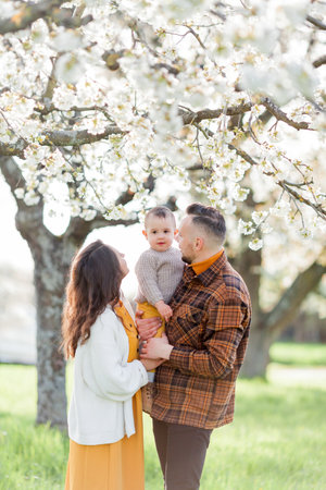 Happy young family with little son walks in blooming garden. Mom and dad with 1 year old baby.の写真素材