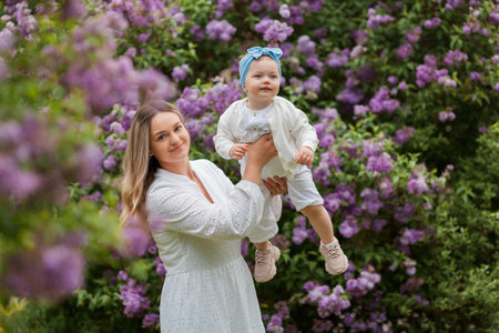 Young beautiful mother with little daughter 1.5 years old in blooming lilacs. Happy family in the park.の写真素材