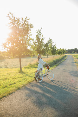 Beautiful young dark-haired woman on picnic in the field. Model in stylish clothes with bicycle.の写真素材