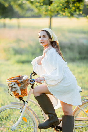Beautiful young dark-haired woman on picnic in the field. Model in stylish clothes with bicycle.の写真素材