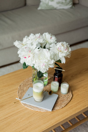 Home cozy interior. Candles, a bouquet of peonies in a glass vase, a glass of matchalate on a wooden coffee table.の写真素材