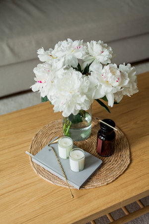 Home cozy interior. Candles, a bouquet of peonies in a glass vase on a wooden coffee table.の写真素材