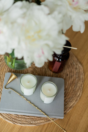 Home cozy interior. Candles, a bouquet of peonies in a glass vase on a wooden coffee table.の写真素材