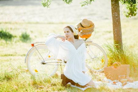Beautiful young dark-haired woman on picnic in the field. Model in stylish clothes with bicycle.の写真素材
