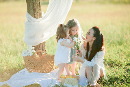 Beautiful young mother with little daughters on a picnic in the field. Summer breakfast with lemons.の写真素材