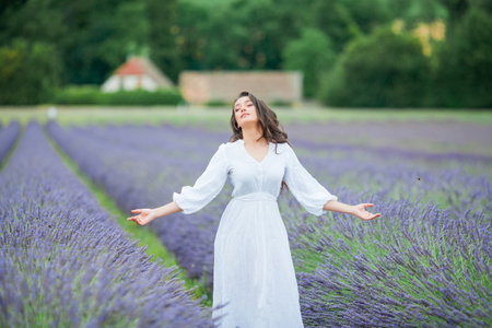 Lavender field. Beautiful dark-haired curly woman in white simple dress in a field of purple flowers.の写真素材