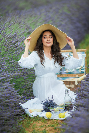 Lavender field. Beautiful dark-haired curly woman in white simple dress in a field of purple flowers.の写真素材