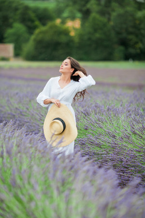 Lavender field. Beautiful dark-haired curly woman in white simple dress in a field of purple flowers.の写真素材