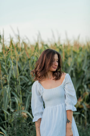 Young beautiful woman 26 years old in white simple dress in summer field. Green corn.の写真素材
