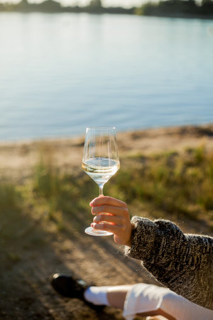 Closeup of glass of white wine in woman's hand. Beautiful young model on an autumn picnic. Sun rays.の写真素材