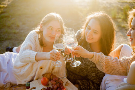 Young beautiful women of 25 years old on an autumn picnic near the lake. Glass of white wine, pastries. Happy models chatting merrily.の写真素材