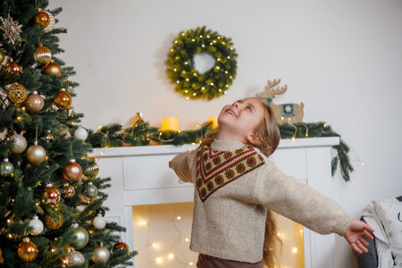 An adorable little girl of 5 years old with long curly hair and blue eyes decorates a Christmas tree. Holidays. New Year.の写真素材