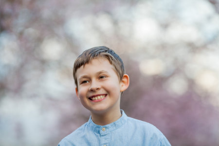 Cute smiling boy walks along the street of cherry blossoms. Happy children. Spring.