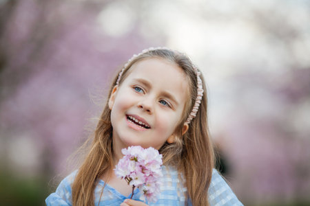 Cute smiling girl is walking along the street of cherry blossoms. Happy children. Spring.