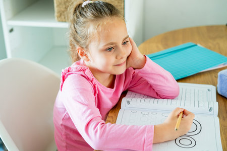 Cute little girl of 6 years old is doing homework at home in the kitchen at the table. Back to school. Cozy.の写真素材