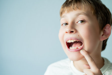 Change of milk teeth. 10 year old boy holds his face with his hand and shows his mouth.の写真素材