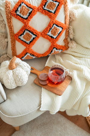 Autumn home decor. Hot tea in glass mug, chocolate cookies, knitted blanket, pillows on chair by the window.の写真素材