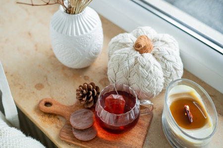 Autumn home decor. Hot tea in glass mug, chocolate cookies, pumpkin, candle on the windowsill.の写真素材