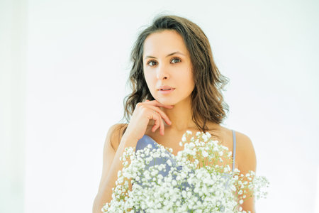 Portrait of young woman with bouquet of white flowers on white background. Model in purple elegant...