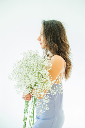 Portrait of young woman with bouquet of white flowers on white background. Model in purple elegant romantic dress. Spring.の写真素材
