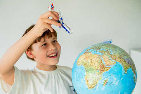 Little boy is looking at the globe with small airplane in his hands. Preparing route for trip....