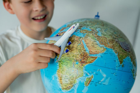 Little boy is looking at the globe with small airplane in his hands. Preparing route for trip....