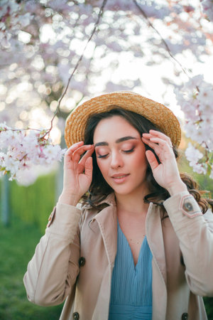 Young beautiful woman 36 years old with curly long dark hair near blooming sakura at sunset. Model...