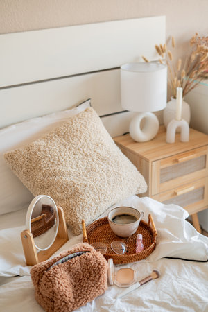 Cup of hot coffee on wicker rattan tray, cosmetics on white bed linen. Spring mood. Home light beige...