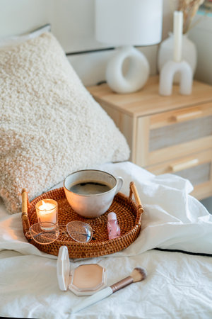 Cup of hot coffee on wicker rattan tray, cosmetics on white bed linen. Spring mood. Home light beige...