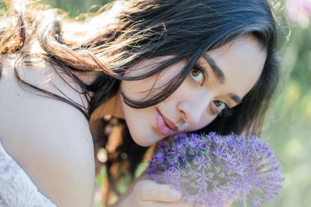 Portrait of a young dark-haired woman near flowers in the park. Happy model in a romantic dress rejoicing in spring.の写真素材