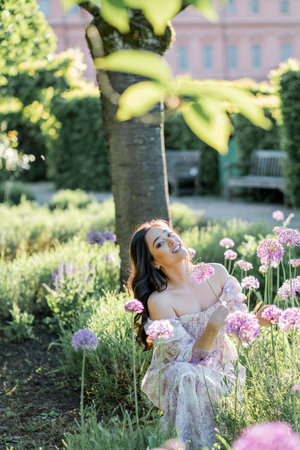 Portrait of a young dark-haired woman near flowers in the park. Happy model in a romantic dress rejoicing in spring.の写真素材