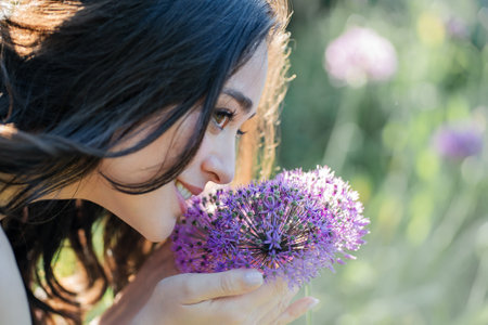 Portrait of a young dark-haired woman near flowers in the park. Happy model in a romantic dress rejoicing in spring.の写真素材