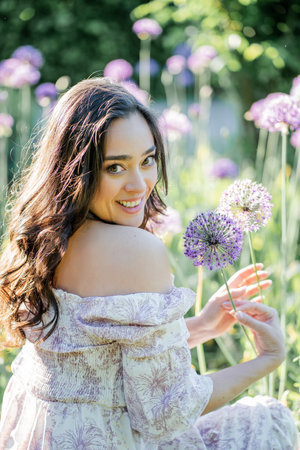 Portrait of a young dark-haired woman near flowers in the park. Happy model in a romantic dress rejoicing in spring.の写真素材