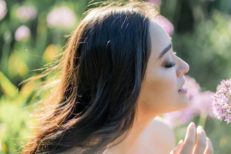 Portrait of a young dark-haired woman near flowers in the park. Happy model in a romantic dress rejoicing in spring.の写真素材