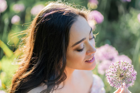 Portrait of a young dark-haired woman near flowers in the park. Happy model in a romantic dress...