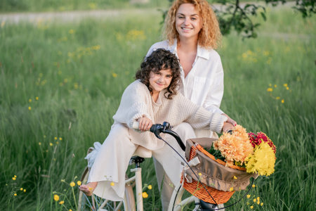 Mother and daughter enjoying a sunny day with a bicycle in a field of flowers. Red-haired young woman with a 5-year-old girl resting in nature.の写真素材