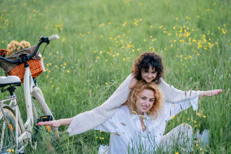 Mother and daughter enjoying a sunny day with a bicycle in a field of flowers. Red-haired young woman with a 5-year-old girl resting in nature.の写真素材