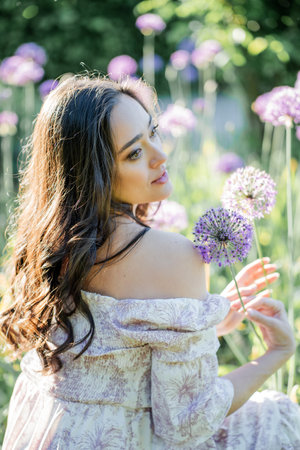Portrait of a young dark-haired woman near flowers in the park. Happy model in a romantic dress rejoicing in spring.の写真素材