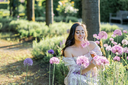 Portrait of a young dark-haired woman near flowers in the park. Happy model in a romantic dress rejoicing in spring.の写真素材