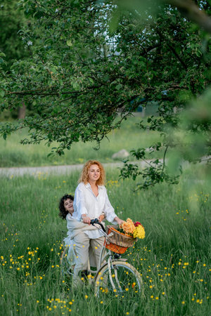 Mother and daughter enjoying a sunny day with a bicycle in a field of flowers. Red-haired young woman with a 5-year-old girl resting in nature.の写真素材